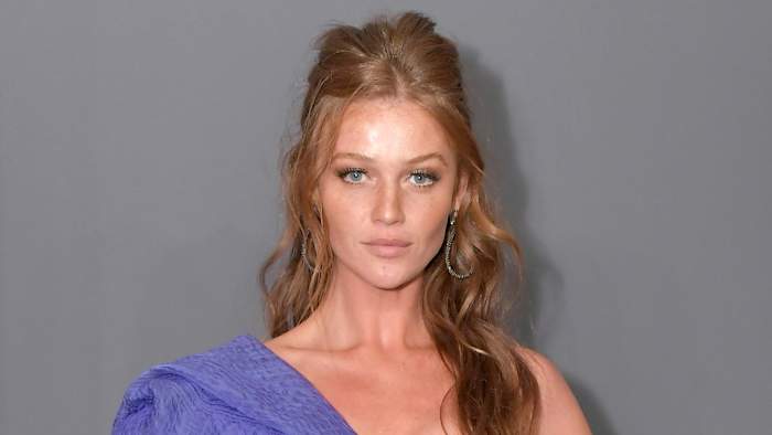 Cintia Dicker poses in a one-shoulder purple dress and wears her red hair in a half updo.